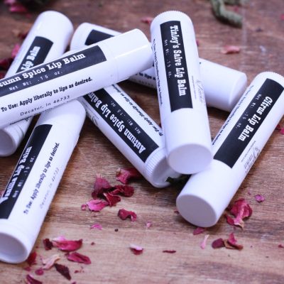 several tubes of lip balm laying in a group on some crushed rose petals